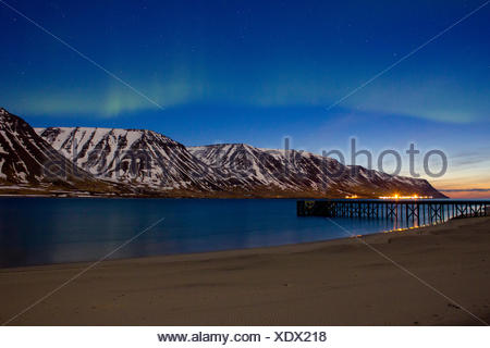 Lumières du nord sur Westfjords avec la ville de Flateyri au loin, l'Islande