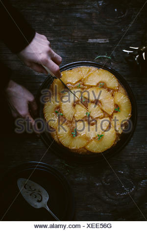 Une femme est de trancher un gâteau d'ananas est photographié par le haut.