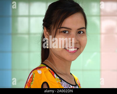 Bellissima giovane donna birmana con macchie di colore bianco giallastro thanaka tradizionale cosmetica viso sulle sue guancie sorrisi per la fotocamera. Foto Stock