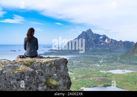 Una preparazione atletica e donna attraente medita l'incredibile paesaggio delle isole Lofoten dalla cima di una montagna sopra la città di Kabelvag e Svolvaer. Foto Stock