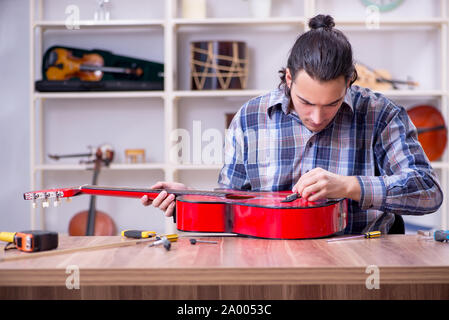Il giovane bello repairman riparazione di chitarra Foto Stock