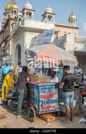 Persone in piedi intorno a un venditore a vendere bevande dal suo carrello al di fuori di una moschea di Nuova Delhi in un pomeriggio caldo. Foto Stock