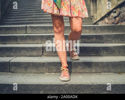 Le gambe di una giovane donna che cammina giù per le scale al di fuori di una città Foto Stock