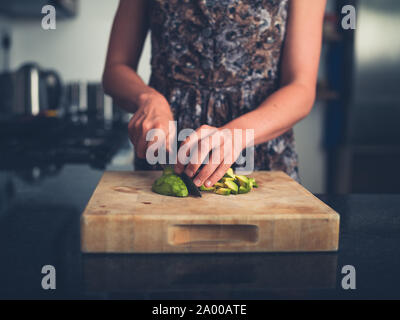 Una giovane donna è la trinciatura avocado nella sua cucina moderna Foto Stock