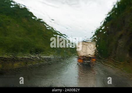 La scarsa visibilità concetto guida. Parabrezza bagnato con heavy rain e via sulla strada sdrucciolevole in anticipo. Le gocce di pioggia sul parabrezza della vettura in movimento su autostrada. Calcolatore ABS Foto Stock