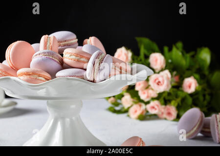 Macarons su un piedistallo bianco. bel bouquet di rose a sfondo nero, vista orizzontale, close-up Foto Stock