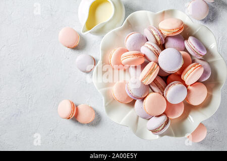 French macarons su una torta di porcellana di stand e creamer su un tavolo in cemento, vista orizzontale, piana, laici dello spazio libero Foto Stock