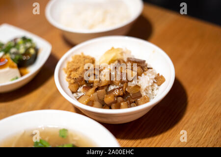 Taiwanese brasati di carne di maiale pancia sul riso in una ciotola bianco su un ristorante in legno Tavolo. Lu Rou 滷肉飯 ventola è uno di Taiwans più popolari piatti nazionali Foto Stock