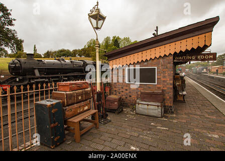 Sala d'attesa sulla piattaforma ferroviaria con treno a vapore dietro e bagagli impilati sulla piattaforma Foto Stock