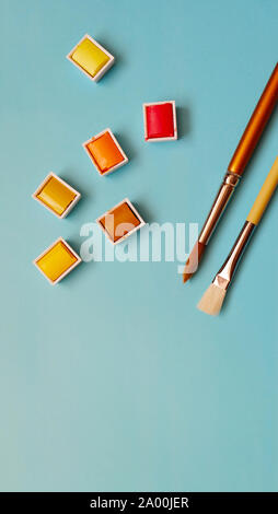 Spazzola di vernice e calda di tavolozze di colori di rosso, arancione e giallo, con sfondo blu. Foto Stock