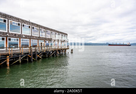 Grigio edificio in legno e il vecchio molo pesca con pali di legno sporgente dall'acqua a bocca larga del fiume Columbia in Astoria city sul Foto Stock