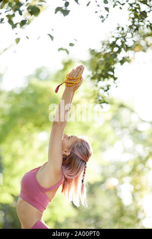 Sporty giovane donna stretching le braccia durante la pratica dello yoga nella natura nel giorno di estate Foto Stock