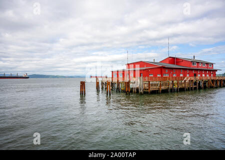 Red commerciali edifici in legno di un vecchio pesca e molo pilota con pali metallici sporgenti dall'acqua a bocca larga del fiume Columbia in Foto Stock
