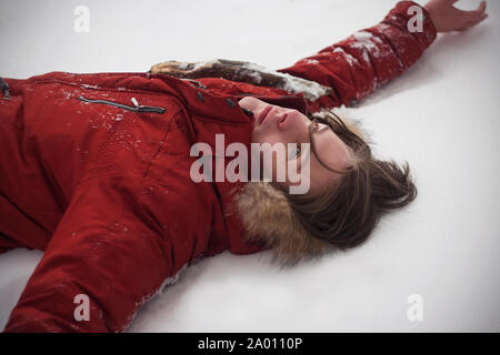 Viaggiare ragazzo in una giacca rossa giacente sulla superficie di un cumulo di neve in inverno freddo con un look vuota. Foto Stock