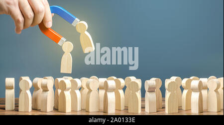 Imprenditore con un magnete tira figure in legno di persone al di fuori della grande folla. Il reclutamento di lavoratori. La formazione di un nuovo team. Ricerca di richieste di persone e Foto Stock