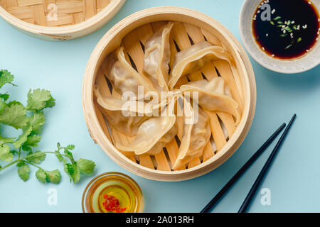 Gyoza gnocchi con anatra cucinata in bambù sistema di cottura a vapore su sfondo blu è servito con salsa di soia e il coriandolo. Vista superiore, laici piatta Foto Stock