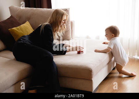 Bionda e giovane madre avente il tempo di qualità con il suo bambino mio figlio a casa famiglia piatto - vestita di nero vestito budoir costume abito di pelo