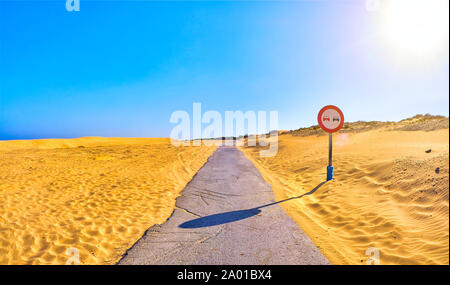 Incrinato strada asfaltata attraversando un arido terreno di dune con un sorpasso non firmare. Foto Stock