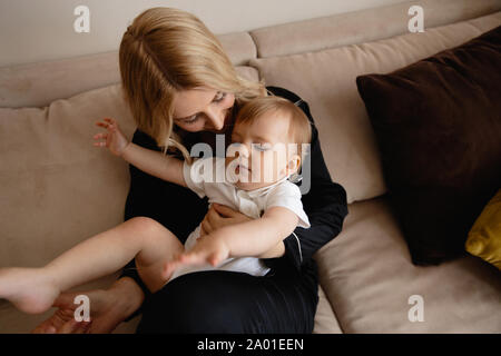 Bionda e giovane madre avente il tempo di qualità con il suo bambino mio figlio a casa famiglia piatto - vestita di nero vestito budoir costume abito di pelo