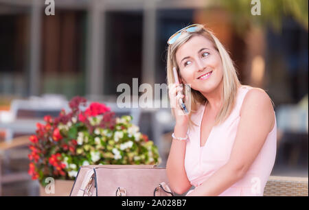 Donna bionda di parlare con qualcuno su un cellulare in un ristorante con terrazzo Foto Stock