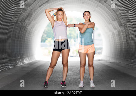 Le donne con fitness trackers stretching all'aperto Foto Stock