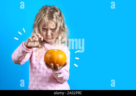 Carino Ragazza strega con capelli biondi evoca oltre una zucca su uno sfondo colorato Foto Stock