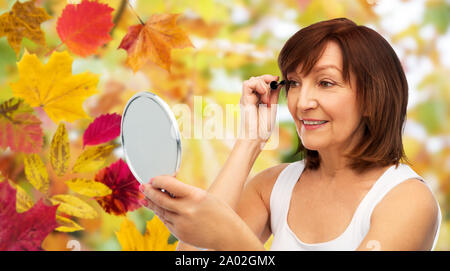 Sorridente donna senior con specchio applicazione di mascara Foto Stock