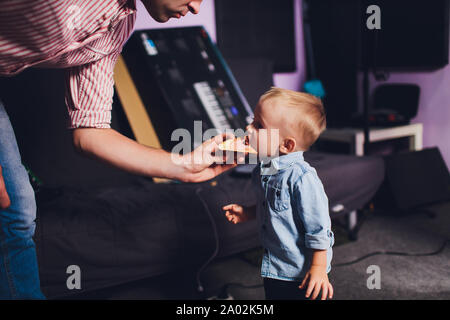 Divertente bionda little Baby girl nel bellissimo abito bianco mordere sul pezzo di gustosa pizza tenendolo fermo con le mani non. Foto Stock