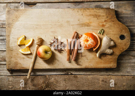 Flatlay con ingredienti per la cottura di vin brulé. Apple, mandarino, bastoncini di cannella, anice stelle, cardamomo e zenzero sul tagliere di legno Foto Stock
