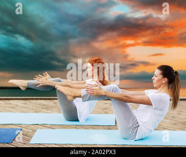 Donne che fanno yoga a mezza barca pongono all'aperto Foto Stock