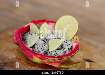 Frutta del drago affettata e fetta di lime in una ciocca di buccia di frutta del drago su sfondo vecchio tavolo di legno. Foto Stock
