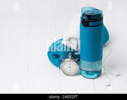 Blu bottiglia di acqua, asciugamani, le cuffie e il cronometro. Attrezzature sportive in bianco sullo sfondo di legno. Palestra per il fitness uno stile di vita sano concetto. Foto Stock