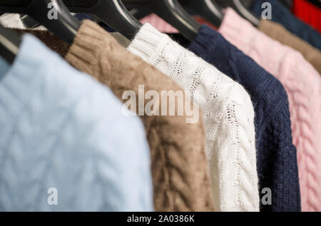 Vari cavo a maglia Maglioni o maglie su hanger rack in un negozio di abbigliamento o in un armadio, il fuoco selettivo Foto Stock