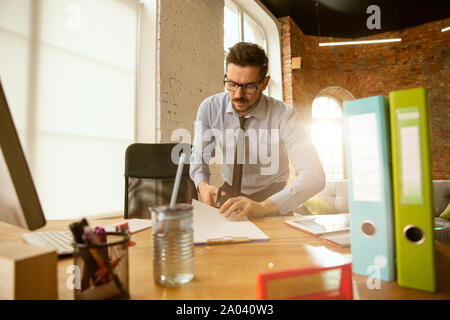 Nel processo. Un giovane imprenditore muovendosi in ufficio, ottenendo un nuovo posto di lavoro. Giovane maschio lavoratore di ufficio equipaggia il nuovo gabinetto dopo la promozione. Sembra felice. Business, lifestyle, nuovo concetto di vita. Il disimballaggio. Foto Stock