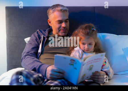 Tempo per la famiglia. Il piacere ragazza appoggiata al suo padre mentre guardando le immagini colorate Foto Stock