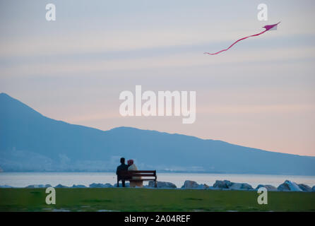 Un giovane seduto sul banco vicino al mare, godendo della vista del mare e di aquilone volante. Izmir, in Turchia. Foto Stock