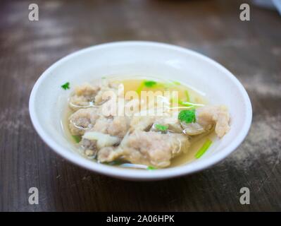 Una piccola ciotola di zuppa di chiara con verde coriandolo e pezzi di maiale fritto on dark tavolo in legno Foto Stock