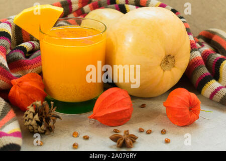 Un bicchiere di fresco succo di zucca e zucca su una tavola decorata con fiori physalis. Un concetto di stagionale sani frullati e succhi di frutta. Foto Stock