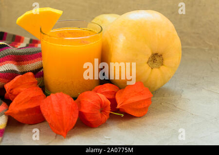 Un bicchiere di fresco succo di zucca e zucca su una tavola decorata con fiori physalis. Un concetto di stagionale sani frullati e succhi di frutta. Foto Stock