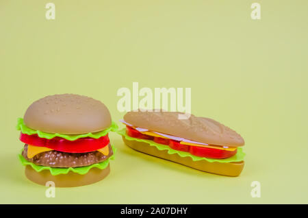 Il fast food. plastica hamburger, hot dog su sfondo giallo Foto Stock