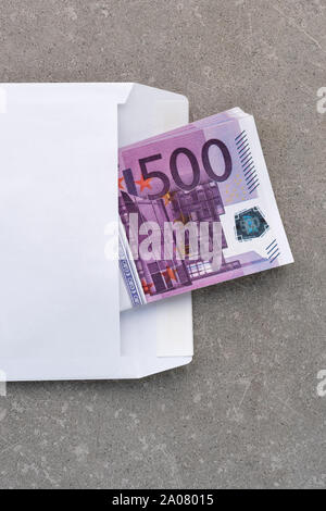 Busta bianca con un 500 euro bills. Pila di cinque centinaia di banconote in euro in apertura busta posta sul cemento. Banconote piegate in una busta come un presente Foto Stock