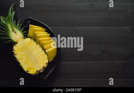 Ananas tagliato in ceramica nera sulla ciotola di legno nero lo sfondo. Copia dello spazio. Foto Stock