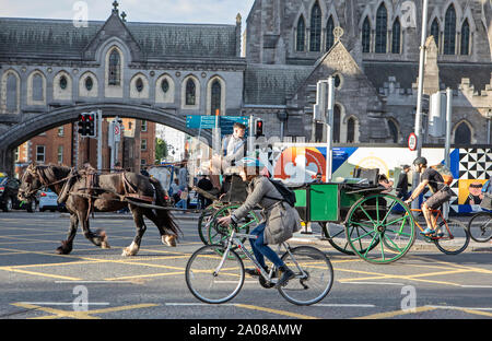 Ciclisti, una carrozza trainata da cavalli, automobili (automobili) e pedoni condividono la strada a Dublino, Irlanda. Foto Stock