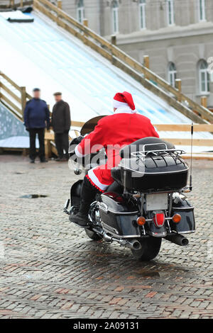 Hip Santa clausola dicendo addio e andare via su una moto, vista posteriore Foto Stock