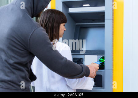 Vista posteriore di un ladro strappi carta dalla donna di mano tramite Bancomat Foto Stock