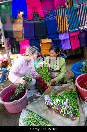 Una femmina caucasica turista che viene rilasciato e una tradizionale birmana mercante donna in un mercato di Nyaung Shwe in Myanmar cercando a livello locale Fl Foto Stock