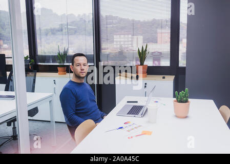 Ritratto di giovane uomo seduto alla sua scrivania in ufficio Foto Stock