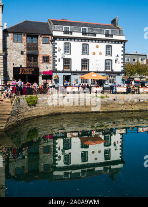 Diners a tavoli fuori le tre corone pub riflessi nell'acqua di Sutton Harbour, Plymouth Foto Stock