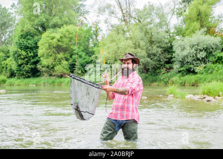 Barbuto brutale fisher la cattura di pesci trote con net. Se regolarmente del pesce si sa come gratificante e rilassante è la pesca. La pesca hobby. La pesca è un sorprendente accessibile ricreativo sport all'aperto. Foto Stock