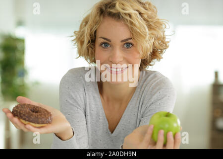 Donna che mantiene mela verde e ciambella Foto Stock